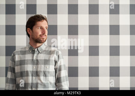Jeune homme avec une barbe, debout devant de papier peint à carreaux et portant une chemise Banque D'Images