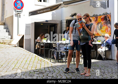 Un homme et femme regardant un Guide livre devant un café tandis que la maman tenant le bébé dans Lisbonne, Portugal Banque D'Images