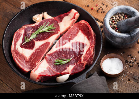 Deux nouvelles matières en viande, Black Angus ribeye steak aux épices dans poêle de fer sur une vieille table rustique. Le boeuf cru sur un fond de bois. Vue d'en haut Banque D'Images