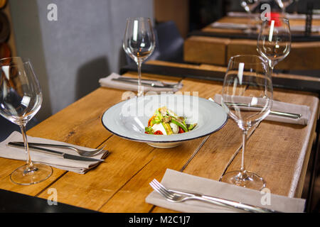 Une table en bois dans le restaurant, servi avec des verres à vin dans le milieu, est un plat végétarien avec légumes et fromage mozzarella salade Banque D'Images