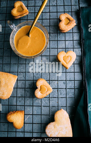 Baking cookies faits maison de la Saint-Valentin, en forme de cœur avec du beurre d'arachides biscuits linzern crème sur un fond de béton gris, vue du dessus. Banque D'Images