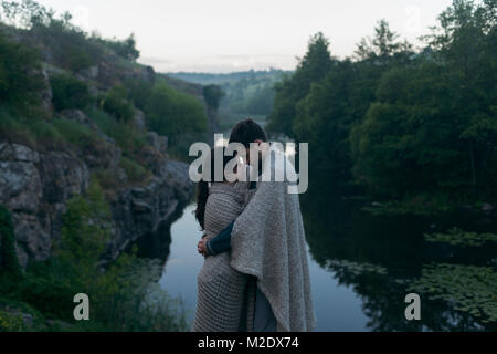 Caucasian couple wrapped in blanket hugging près de river Banque D'Images