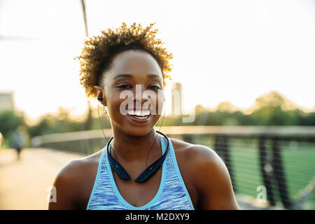 Smiling mixed race woman listening to écouteurs sur bridge Banque D'Images