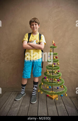 Portrait of Caucasian boy standing près de petit arbre de Noël artificiel Banque D'Images