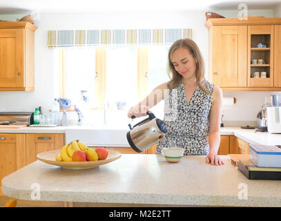 Caucasian woman penché café de pot dans la cuisine Banque D'Images