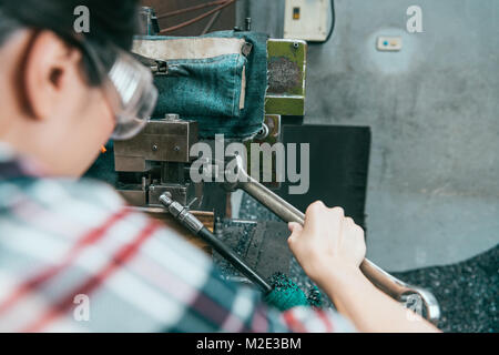 Vue arrière de l'employé d'usine femelle portant des lunettes de sécurité à l'aide de l'outil clé de la réparation de l'appareil de la fraiseuse. selective focus photo. Banque D'Images