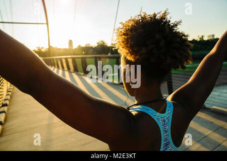 Mixed Race woman stretching arms écouteurs sur bridge Banque D'Images
