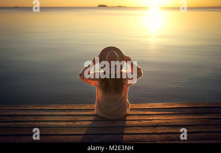 Caucasian woman sitting on dock du lac en admirant le coucher du soleil Banque D'Images