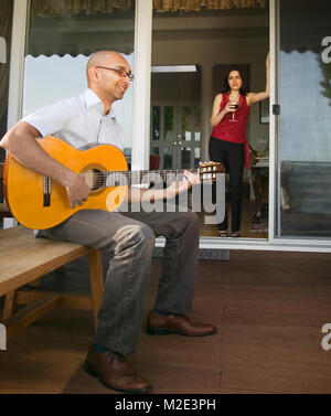 Femme regardant l'homme assis sur un banc à jouer de la guitare Banque D'Images