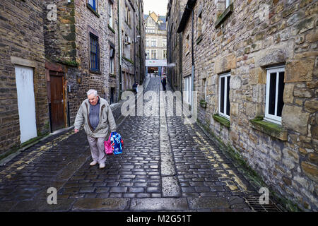 Un pensionné porte son shopping dans une rue pavée humide à Lancaster, Lancashire Banque D'Images
