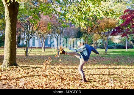 Adolescent avec des cheveux verts coups de feuilles mortes en l'air dans un parc vide avec beaucoup de feuilles sur le sol Banque D'Images