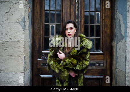 Brunette girl in green manteau de fourrure contre vieilles portes en bois. Banque D'Images