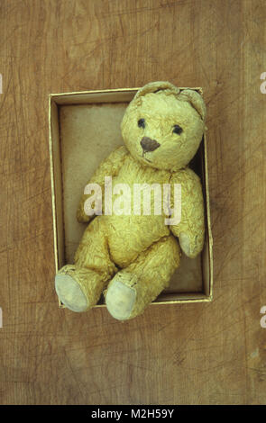 Bien usé Vintage doré pâle ours couché dans la case qui est trop petit Banque D'Images
