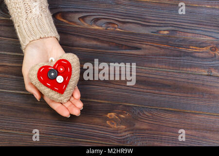 Woman's hands avec de belles étoffes précise cœur rouge. Chandail tricoté confortable blanc sur fond de bois. Concept de donner de l'aide. Concept d'amour avec co Banque D'Images