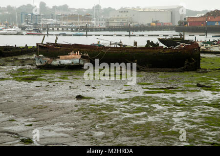 Itchen River, Southampton, à marée basse. Prises de la Northam Pont. Deux vieux bateaux délabrés au premier plan et un parc à ferrailles dans l'arrière-plan Banque D'Images