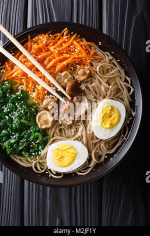 Soupe de nouilles de sarrasin avec des légumes, des champignons shiitake, des oeufs et de close-up de sésame dans un bol. Haut Vertical Vue de dessus Banque D'Images