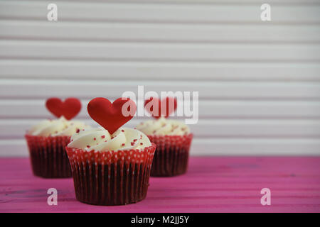 De l'alimentation romantique cupcakes avec white buttercream swirl topping et rouge en forme de coeur amour décorations pour la saint valentin ou un mariage Banque D'Images