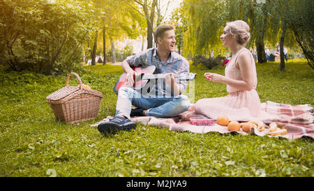 Cheerful girl joyeusement en chantant des chansons avec son mec qui joue de la guitare, date Banque D'Images