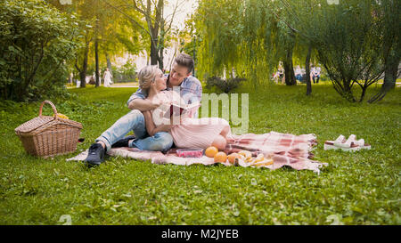 Couple d'offres discuter livre, assis sur un tapis au cours de pique-nique, date romantique Banque D'Images