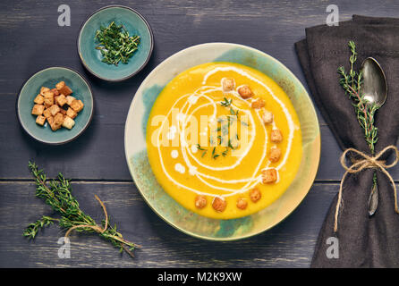 Crème de potiron soupe dans Bol en céramique servi avec croûtons, le thym et la crème sur le bois foncé, vue d'en haut. Banque D'Images