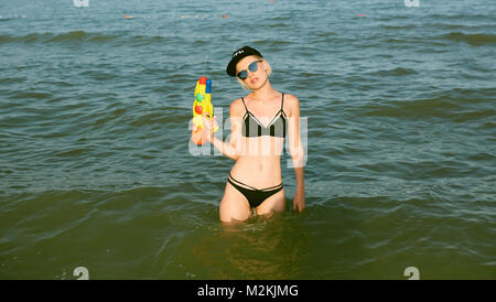 Happy young woman dans un bouchon avec le mot reine jouant avec canon à eau. Effet du film Banque D'Images