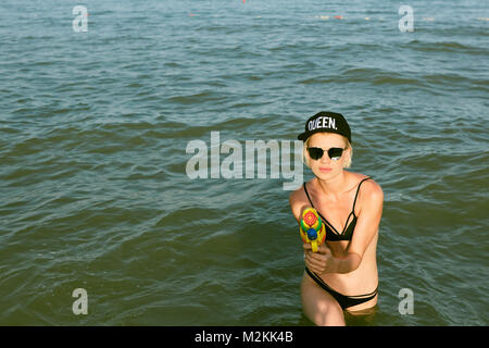 Happy young woman dans un bouchon avec le mot reine jouant avec canon à eau. Effet du film Banque D'Images