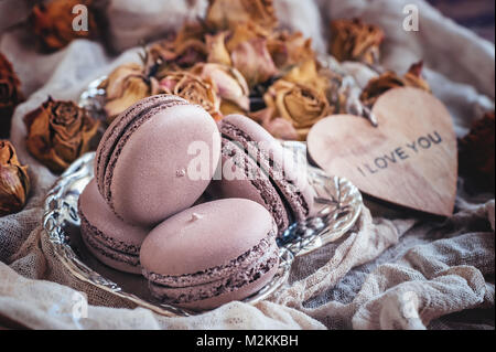 Des petits macarons sur une plaque de métal avec des petites fleurs et un coeur en bois . Focus sélectif. Close up. Banque D'Images