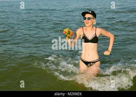 Happy young woman dans un bouchon avec le mot reine jouant avec canon à eau. Effet du film Banque D'Images