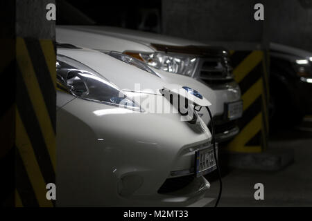 Kiev, Ukraine - le 10 octobre 2017 : voiture électrique Nissan LEAF à charge d'un parking souterrain. L'essence de carburant voiture sur l'arrière-plan. Fiche d'alimentation connectés. Fu Banque D'Images