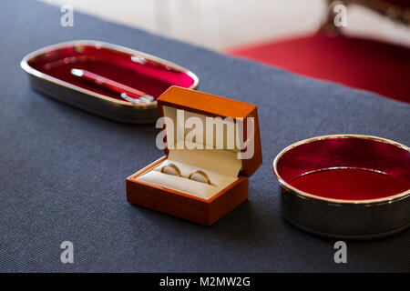 Deux brillants d'or de mariage ensemble de nouveaux mariés mariés dans un beau cercueil en bois brun petite main près de stylo en métal sur la table bleu Banque D'Images