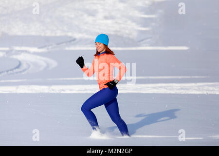 Une jeune femme dans le bleu de l'hat, un chandail orange et le wapiti jupes traverse la neige de l'hiver par un beau jour d'hiver Banque D'Images