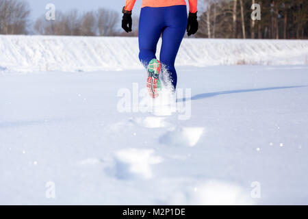 Close-up of a young woman dans des leggings et sneakers qui traverse l'hiver la neige sur un jour d'hiver lumineux, vue arrière. À la suite d'un s Banque D'Images