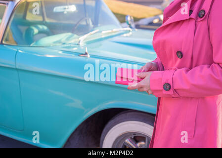 Femme en robe rose chaud holding wallet regardant bébé bleu classic car Banque D'Images