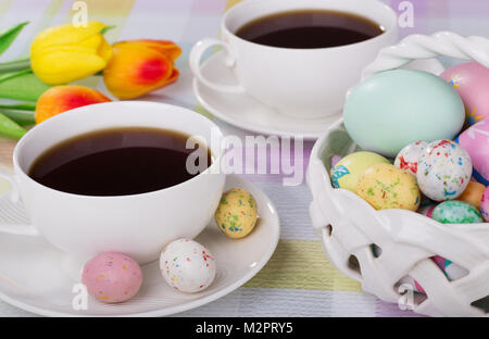 Tasse de café avec des bonbons de Pâques sur une soucoupe à côté d'un panier d'œufs et de bonbons Banque D'Images