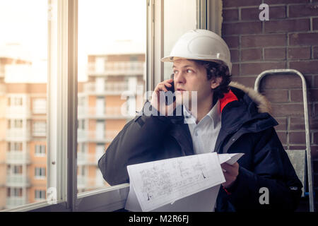 Portrait de concernés disent non rasé builder par mobile tout en gardant des projets différents dans la main. Concept de communication et de travail. Soft focus, tonique. Banque D'Images