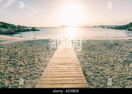 Un chemin mène à travers bois de la plage de sable directement dans la mer et dans le coucher du soleil. Banque D'Images