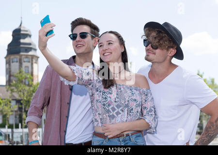 Deux jeunes hommes et une jeune fille près de la ville, Smartphone, semi-portrait Selfies Banque D'Images