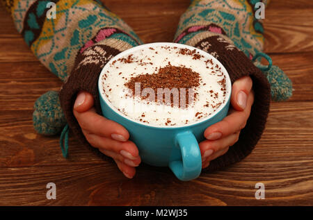 Close up femme deux mains tiennent et Big hug pleine tasse de Cappuccino, Latte avec coeur en chocolat sur mousse de lait sur la table en bois brun, haut Banque D'Images