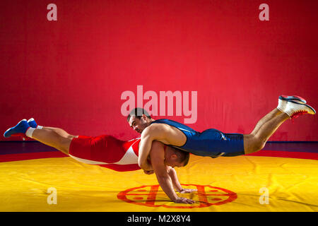 Deux jeunes hommes en bleu et rouge wrestling tights faire un warm-up pour la lutte dans la lutte sports hall Banque D'Images