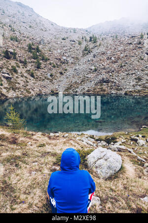 Homme Randonnée dans les montagnes se détendre devant à un lac silencieux en italie - Aoste Banque D'Images