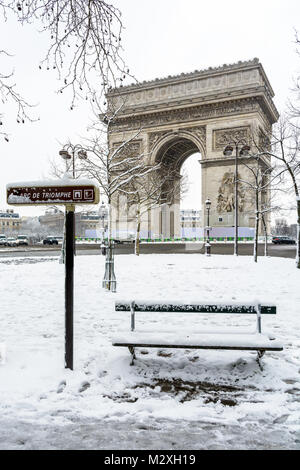 L'hiver à Paris dans la neige. L'Arc de Triomphe avec un banc public couvertes de neige au premier plan. Banque D'Images