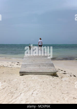 Jeune homme marchant à l'extrémité de la jetée de bois blanchie off Bodden Town Road, Grand Cayman, îles Caïmans. Banque D'Images