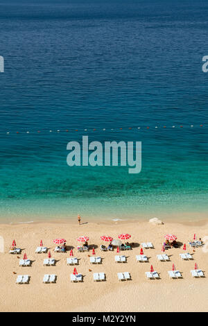 Une vue aérienne d'une belle plage aux eaux turquoises, avec des rangées de chaises longues et des parasols rouges soigneusement disposés sur le rivage de sable. Banque D'Images