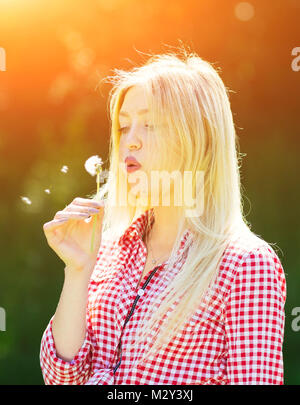 Belle jeune femme soufflant des semences d'un pissenlit fleur Banque D'Images