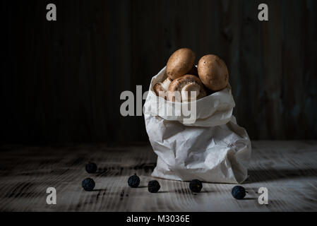 Photo horizontale avec plusieurs brown de champignons comestibles. Les champignons sont en sac de papier blanc. Sac est sur vintage wooden board avec blackthorns renversé. Banque D'Images