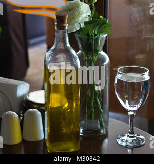 Une bouteille d'huile d'olive sur une table. Deux verres d'eau. Vase avec fleurs. Le grenier à sel Banque D'Images