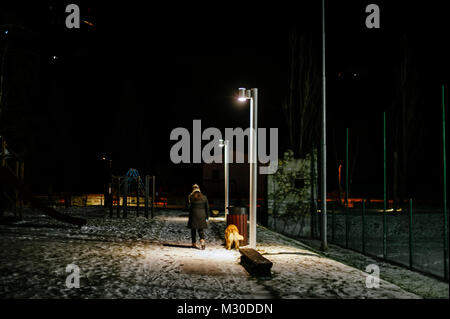 Woman with hat marches le soir avec le chien en laisse, éclairé par la lumière d'une lampe de rue, sur la rue Banque D'Images