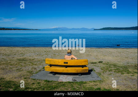 Femme assise sur un banc et bénéficie d les eaux bleues du lac Taupo avec le Parc National de Tongariro en arrière-plan, l'Île du Nord, Nouvelle-Zélande, M. Banque D'Images