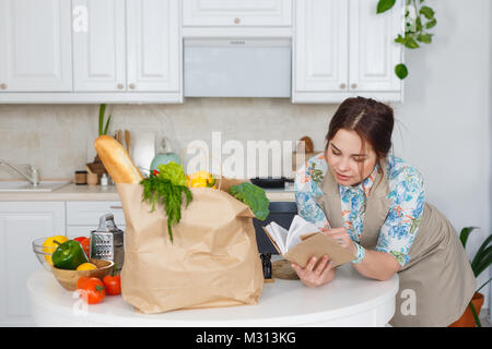 Jeune femme au foyer avec recueil de recettes dans la cuisine Banque D'Images