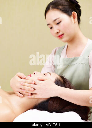 Young Asian masseur effectuant massage visage sur femme dans spa salon Banque D'Images